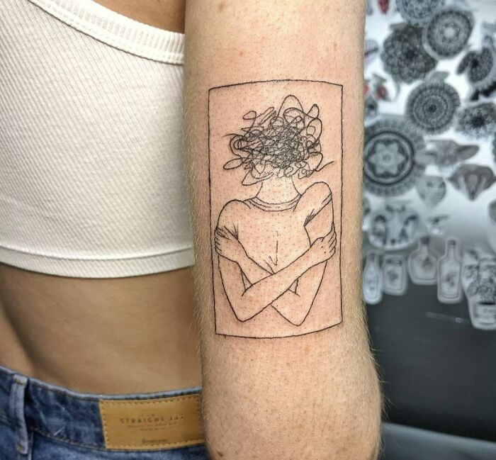 Minimalist tattoo of a person hugging themselves with a scribbled head, symbolizing mental health challenges and healing.