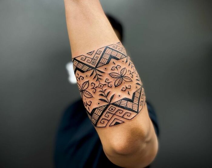 Arm with intricate tribal tattoo design featuring geometric and floral patterns.