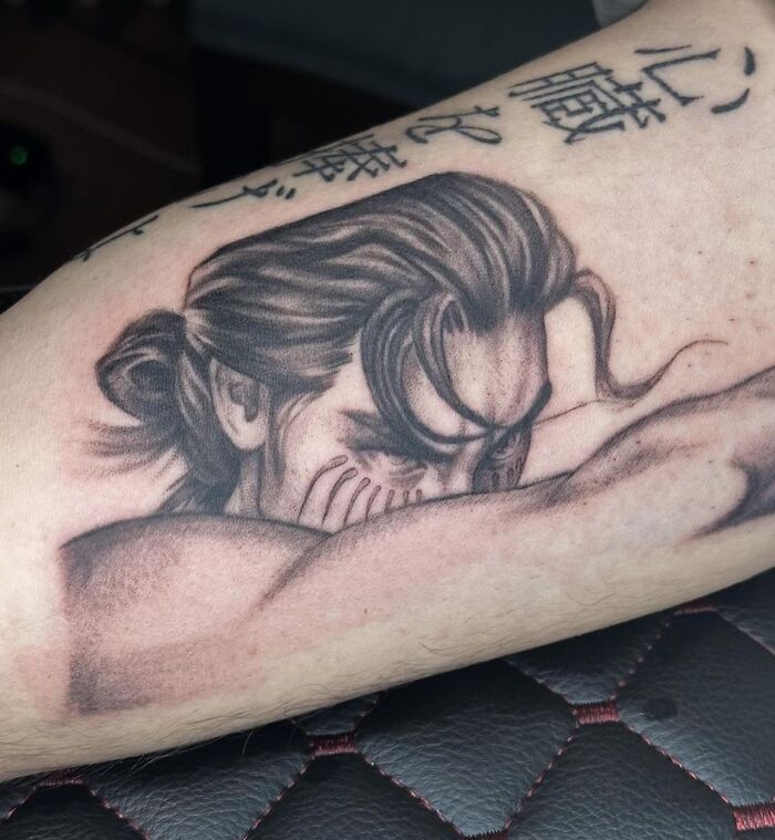 Anime tattoo of a character with long hair and Japanese text on forearm.