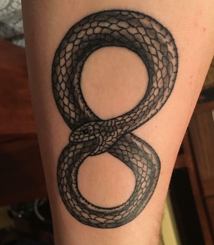 Snake infinity tattoo on arm showcasing eternal creativity.