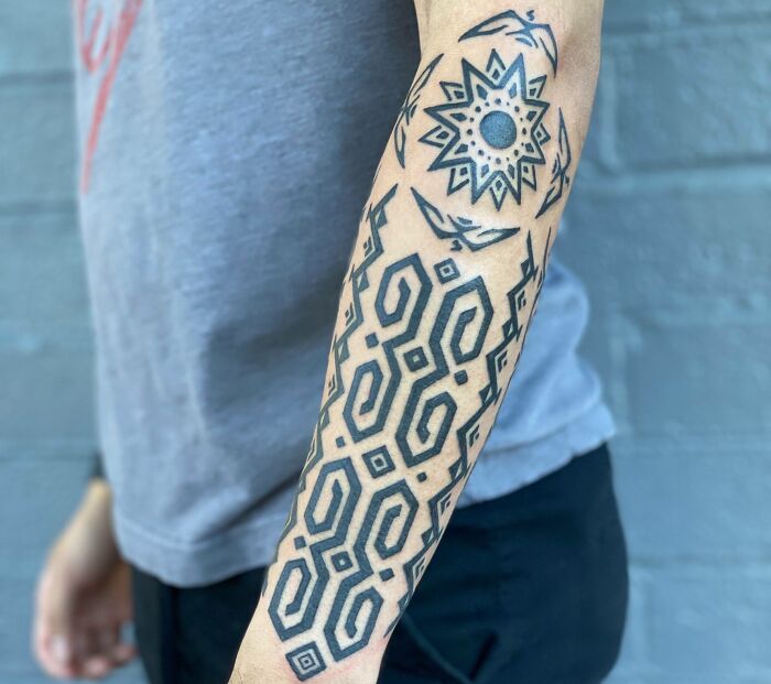 Arm with intricate tribal tattoo design against a gray background.
