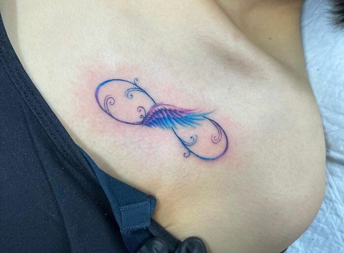 Infinity tattoo with colorful wings on collarbone.