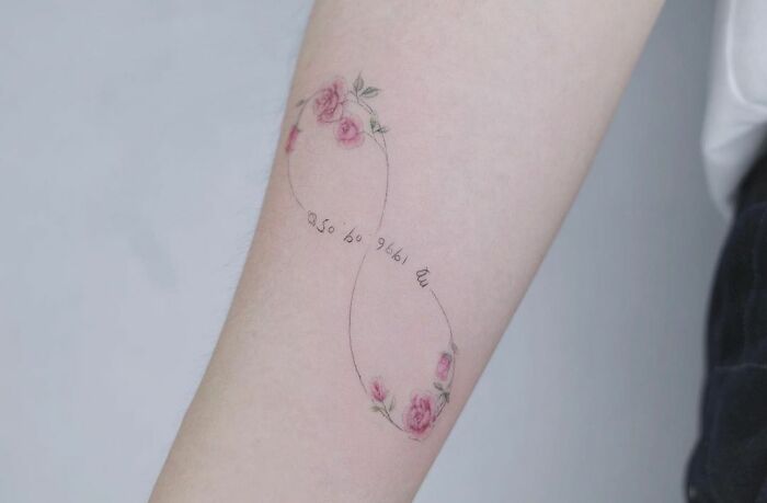 Infinity tattoo with delicate pink roses and script on forearm, symbolizing eternal creativity.