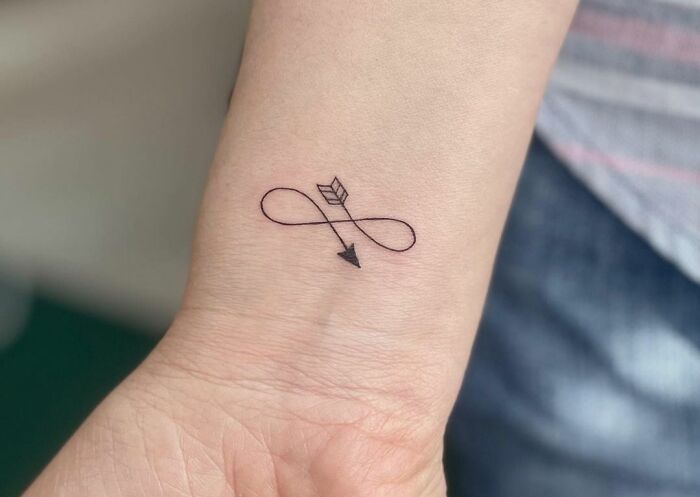 Infinity tattoo with arrow on wrist, symbolizing eternal creativity.