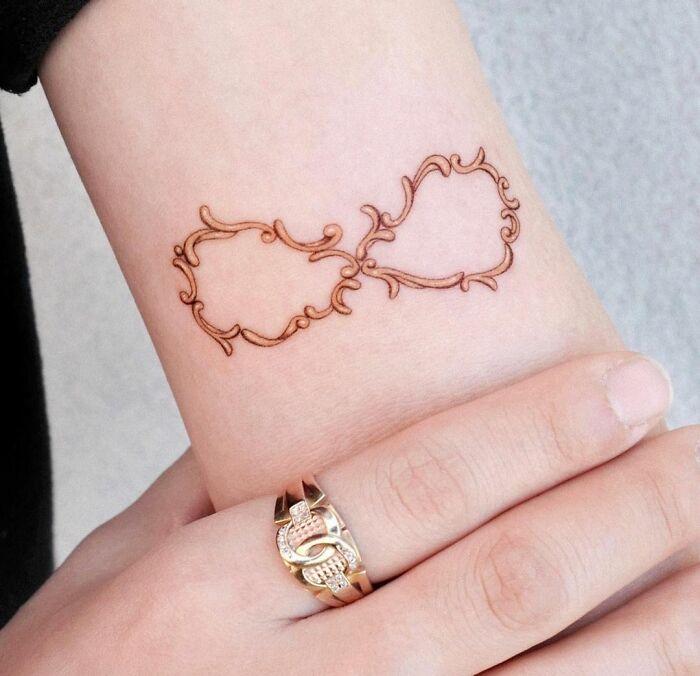 Ornate infinity tattoo on wrist, highlighting creativity and eternity with a unique design, next to a gold ringed hand.