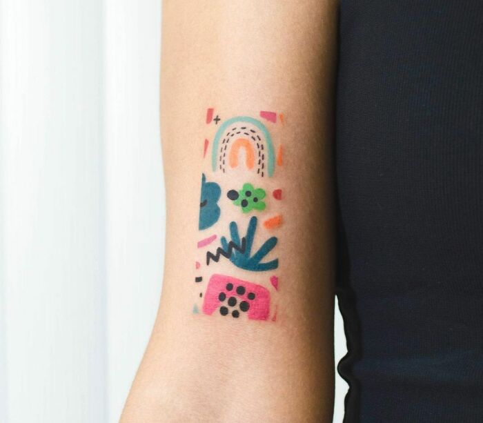Abstract tattoo on forearm featuring colorful geometric shapes and artistic designs.