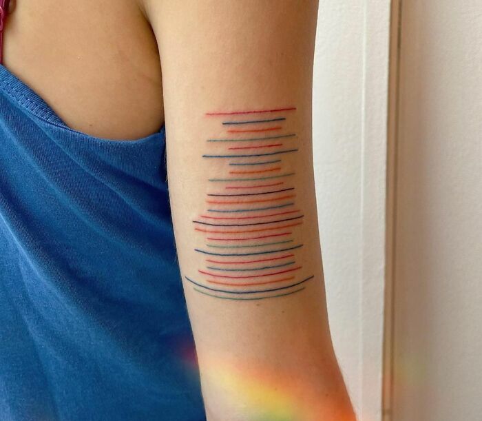 Abstract tattoo on arm with colorful horizontal lines, showcasing artistry and self-expression.