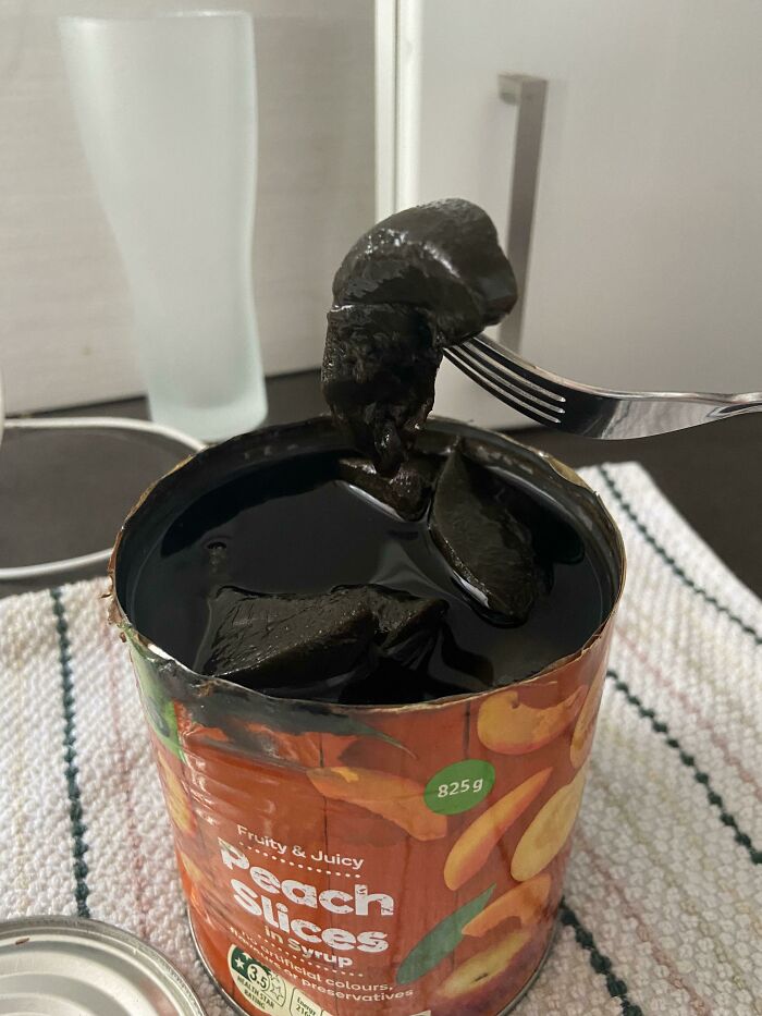 Open can of peach slices with black liquid and blackened fruit pieces lifted by a fork, weirdest pics in an online group.
