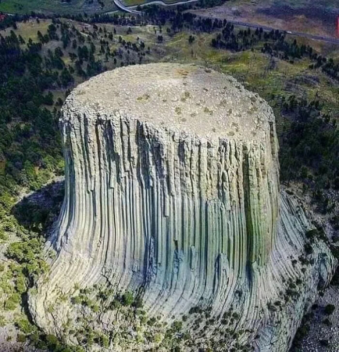 Aerial view of a unique rock formation with vertical grooves surrounded by forest, showcasing one of the weirdest pics.