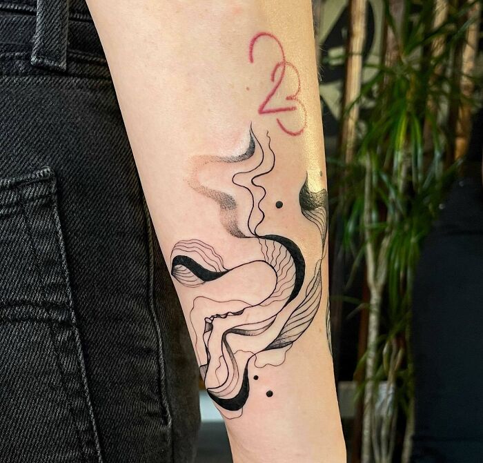 Abstract tattoo on forearm with fluid black lines and red numbers, showcasing artistry and self-expression.