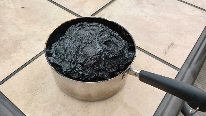 A saucepan filled with a strange, black, tar-like substance sits on a tiled surface, showcasing weirdest pics content.