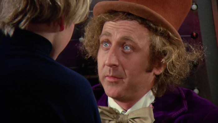 W***y Wonka wearing a brown top hat talking to Charlie, capturing a moment of inspiration and magic.