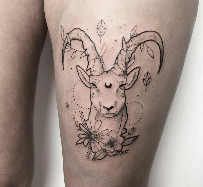 Zodiac tattoo of a goat with floral and celestial designs on a person's thigh.