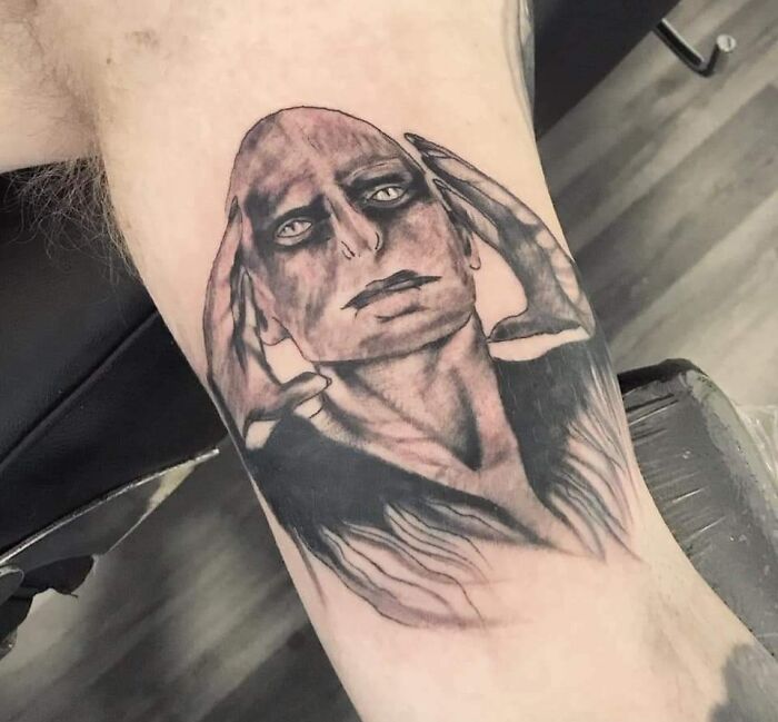 Unique tattoo design of a face with hands on a forearm, highlighting a permanent inking mistake.