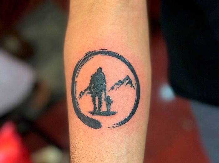 Family tattoo with silhouettes inside a circle, featuring mountains in the background, on forearm.