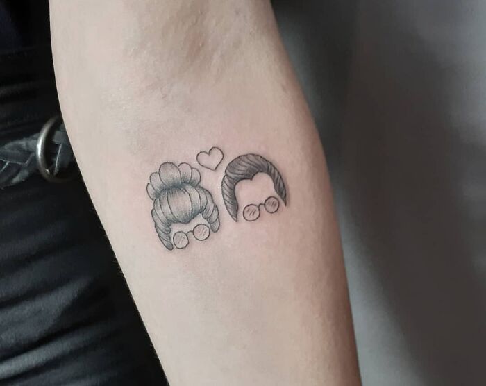 Minimalist tattoo on arm symbolizing family with two faces and a heart.