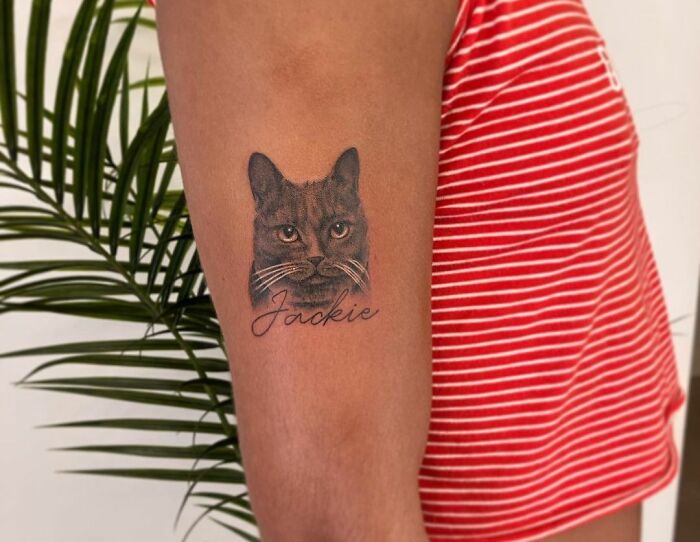 Tattoo of a cat and the name "Jackie" on an arm, symbolizing family honor.