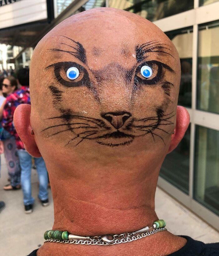 Bald head with a permanent cat face tattoo, complete with googly eyes.