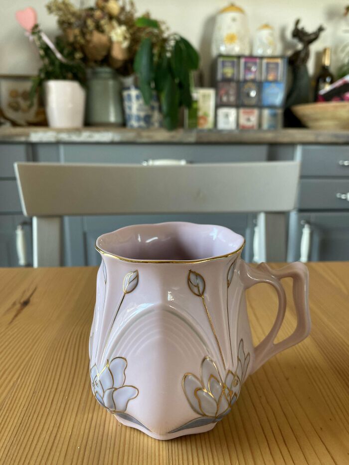 Elegant ceramic mug with floral and gold detail sitting on a wooden table in a cozy kitchen setting.