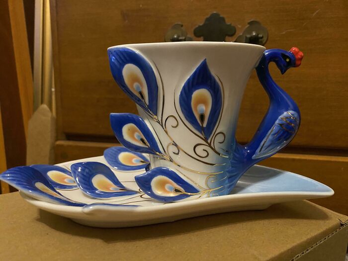 Decorative peacock-themed mug with detailed blue and gold feathers on matching ceramic tray, showcasing unique mug life design.