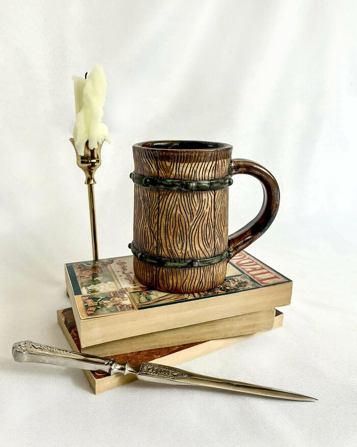 Ceramic mug with wood grain design sitting on books next to a melted candle and ornate letter opener in a cozy setup.