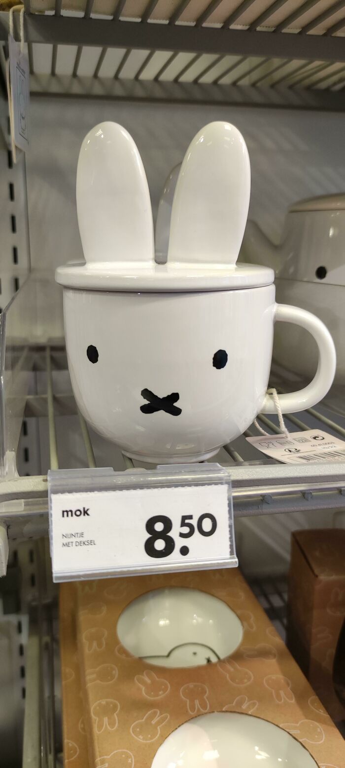 White ceramic mug with bunny ears lid and simple face design displayed on a shelf with price tag.