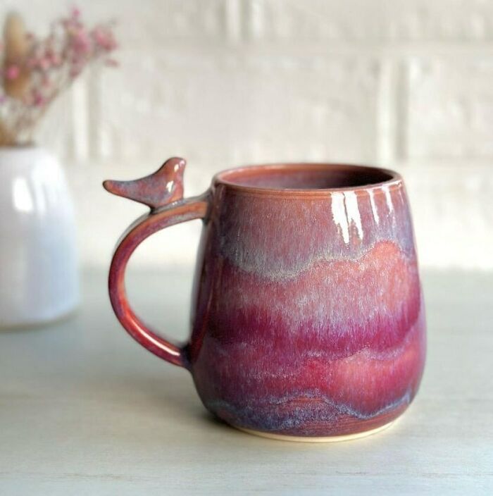 Ceramic mug with a bird-shaped handle in purple and red hues, showcasing unique design beyond typical mug use.