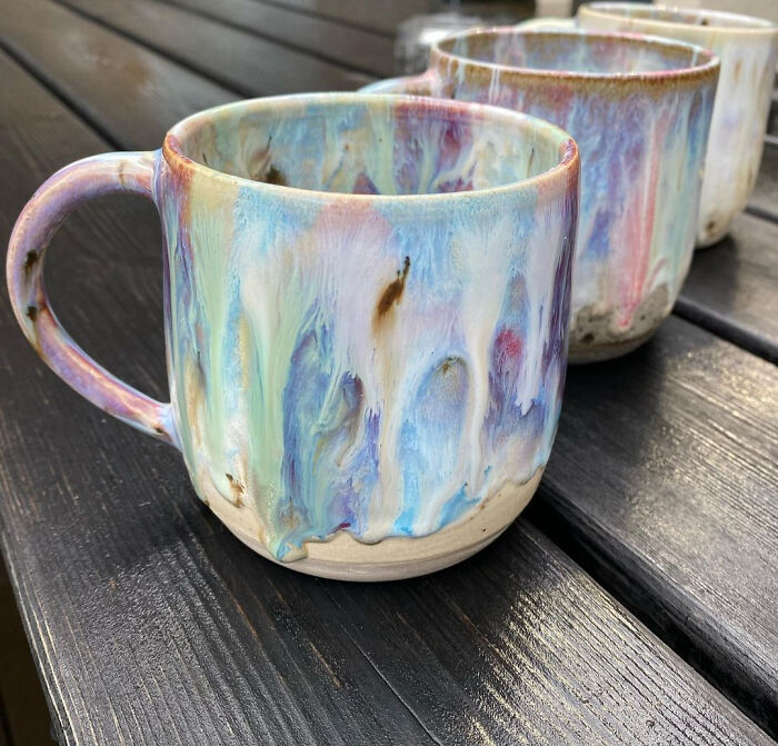 Handcrafted ceramic mugs with colorful glaze patterns lined up on a dark wooden surface, showcasing mug life design.