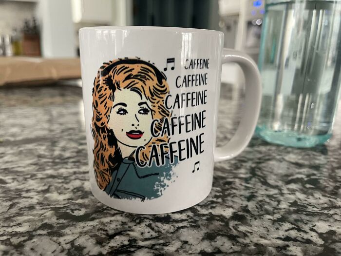 White mug with retro woman illustration and repeated word caffeine, placed on gray granite countertop, showcasing mug life.