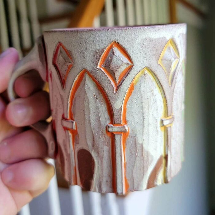 Handcrafted ceramic mug with intricate geometric designs held in hand, showcasing unique mug life creativity.