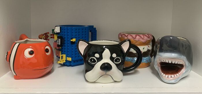Colorful mug life collection featuring fish, dog, shark, donut, and building block designs on a white shelf display.