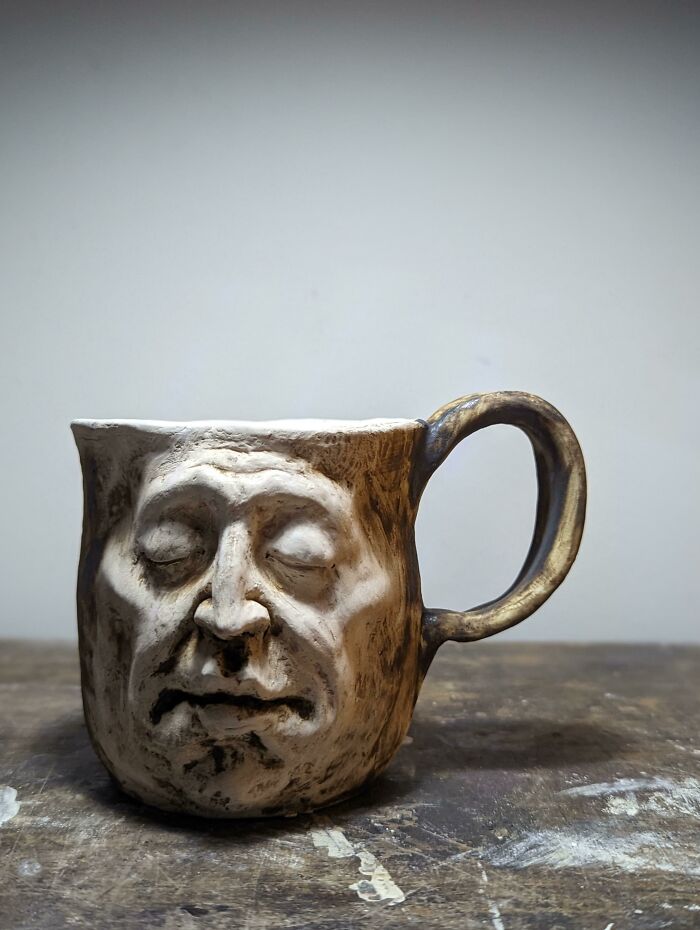 Unique mug with a detailed human face design, showcasing creative mug life art on a wooden surface with a plain background.