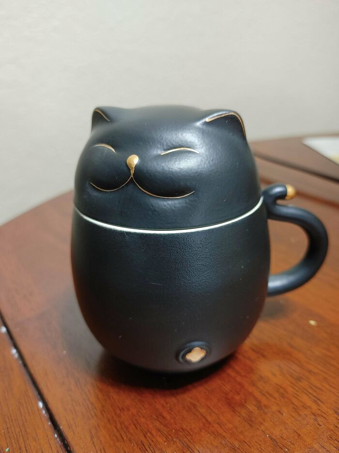 Black cat-shaped mug with gold accents sitting on a wooden surface, showcasing creative mug life design and function.