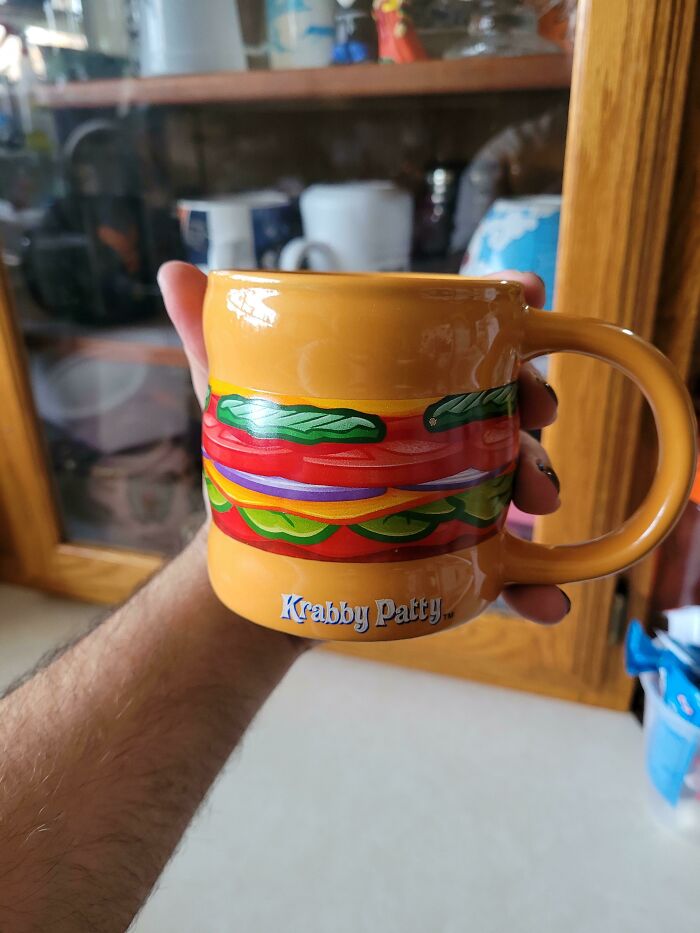 Hand holding a colorful Krabby Patty mug with sandwich design, showcasing creative mugs that serve beyond their initial purpose.