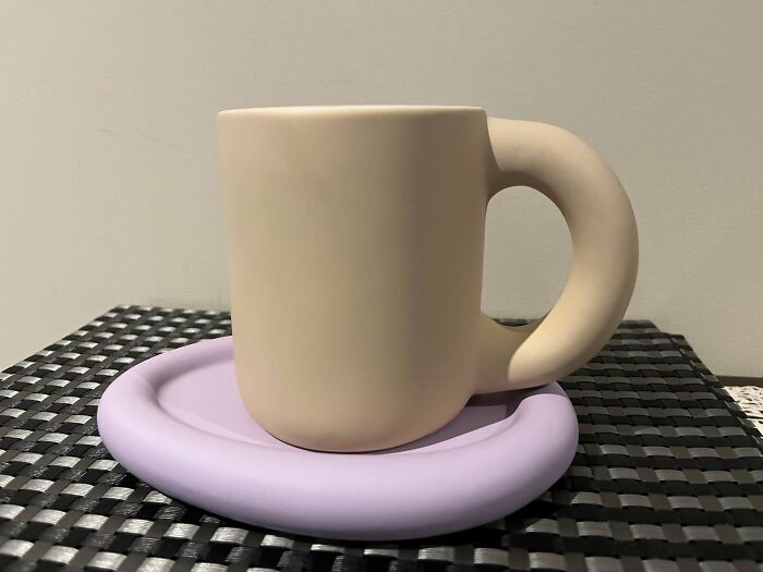 Beige mug with a large handle sitting on a purple coaster on a black textured surface showcasing creative mug life design.
