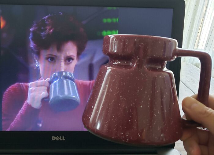 Person holding a unique speckled brown mug in front of a laptop screen showing a woman drinking from a similar mug.