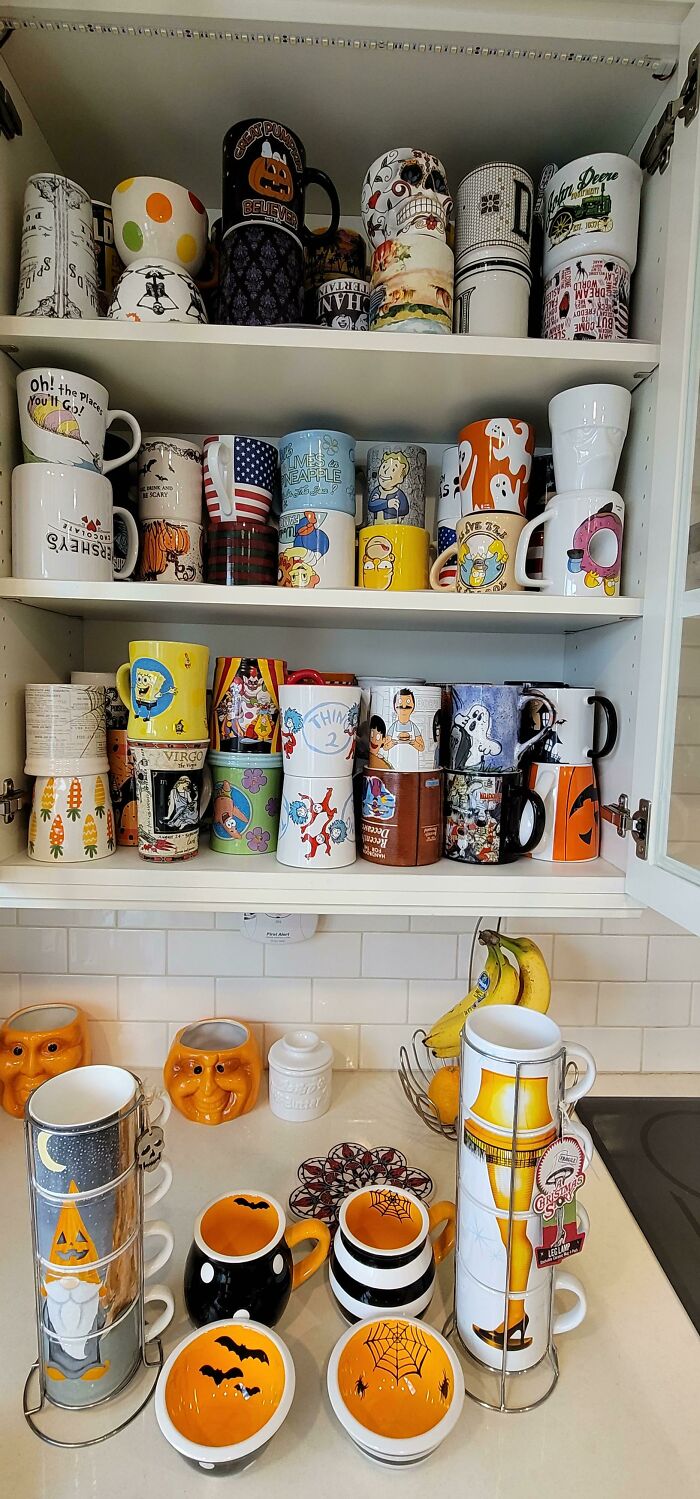 Colorful and themed mugs displayed in a kitchen cabinet and on a countertop, showcasing unique mug life designs.