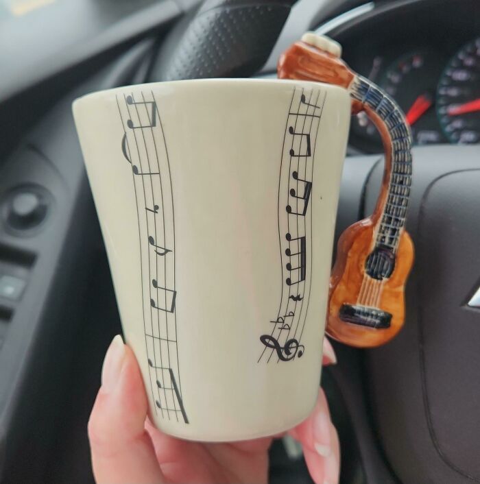 Hand holding a music note mug with a guitar-shaped handle inside a car, highlighting creative mug life design.