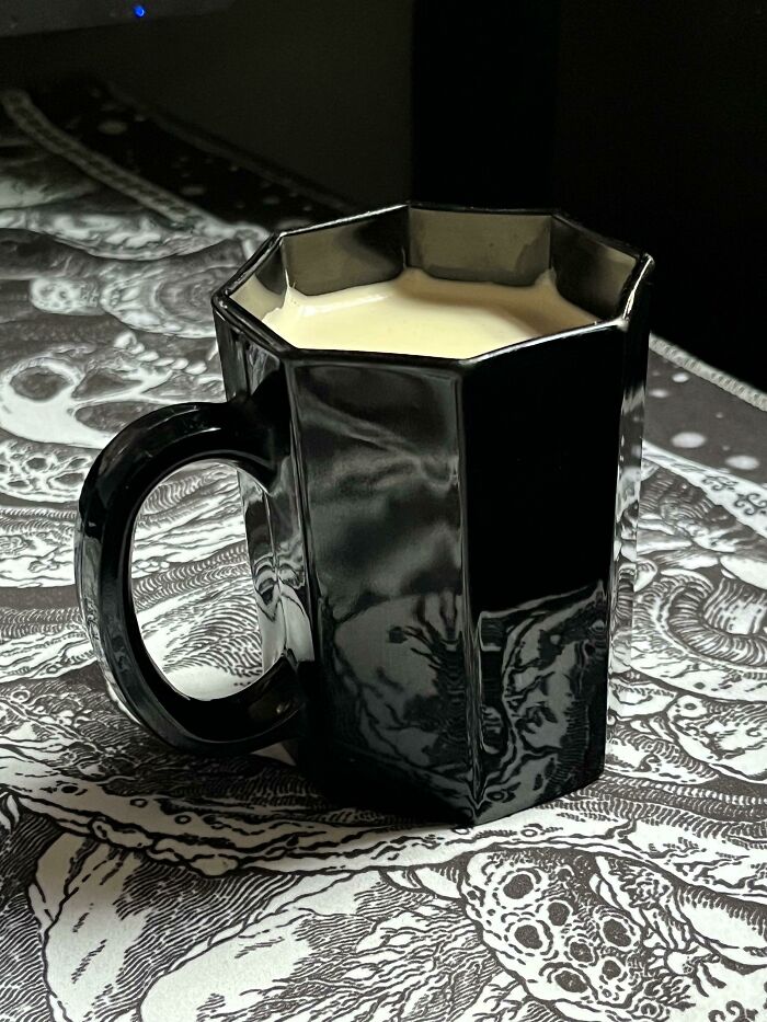Black octagonal mug filled with cream, placed on a detailed monochrome patterned surface, showcasing unique mug life design.
