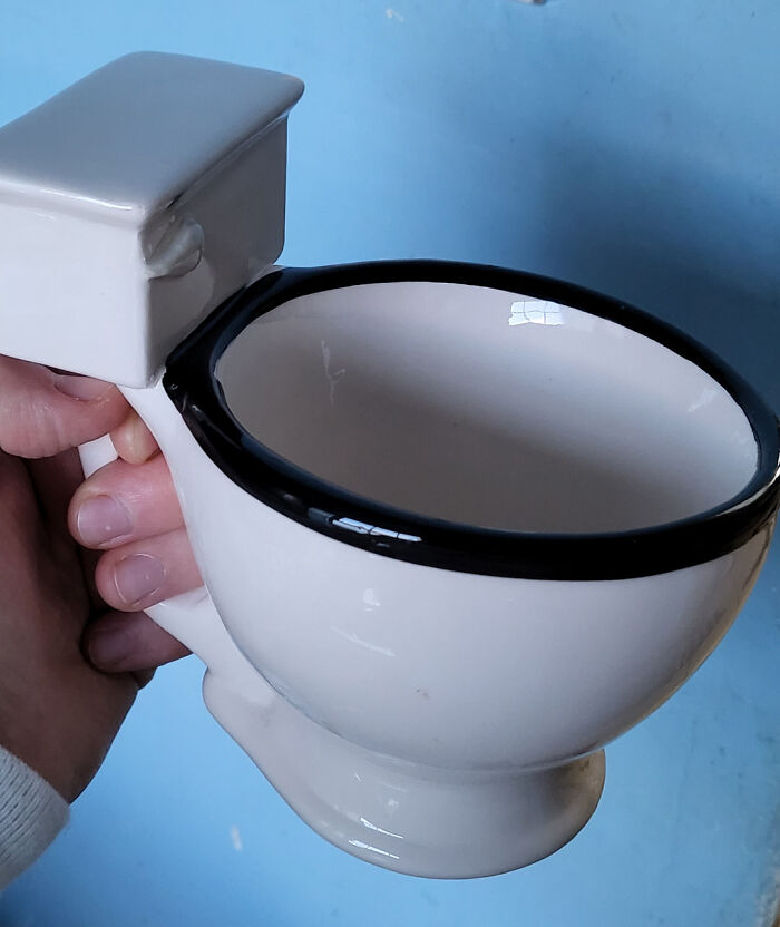 Hand holding a ceramic mug shaped like a toilet bowl, showcasing a unique and funny mug life design.