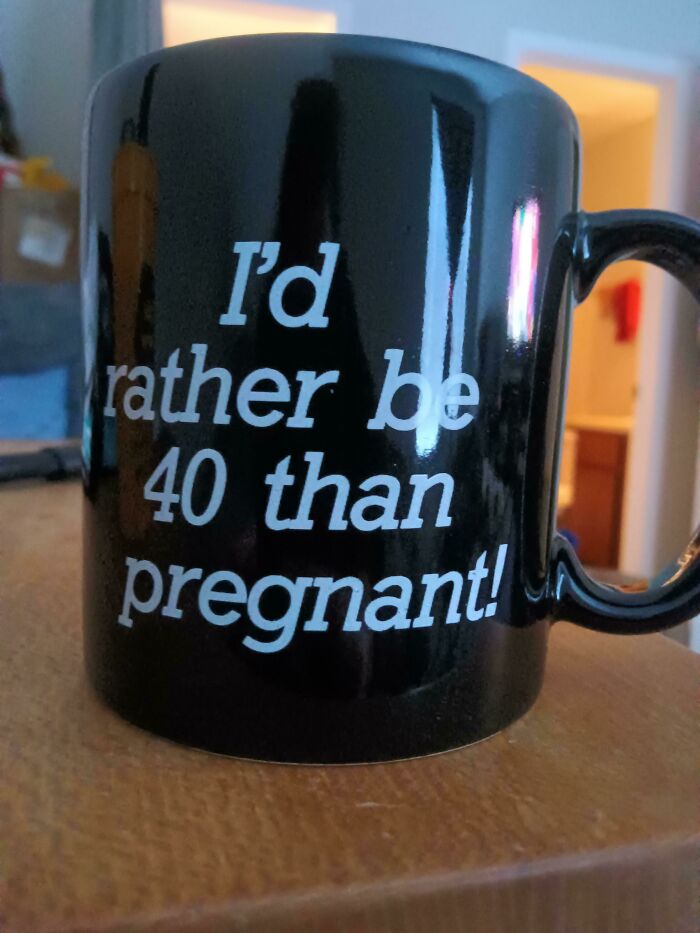 Black mug with white text saying "I'd rather be 40 than pregnant" placed on a wooden surface, showcasing a mug life design.