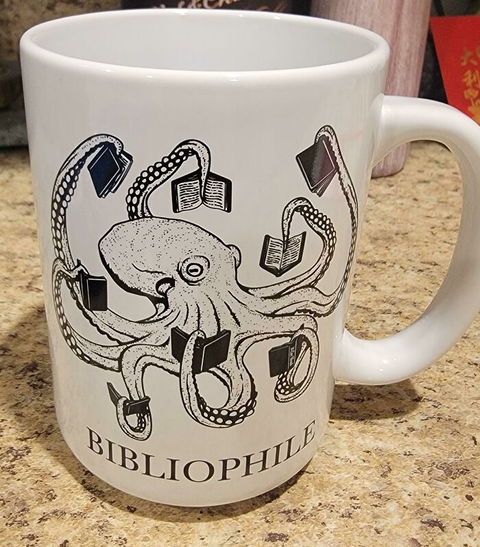 White mug with an octopus holding books on its tentacles and the word bibliophile printed below, showcasing unique mug design.