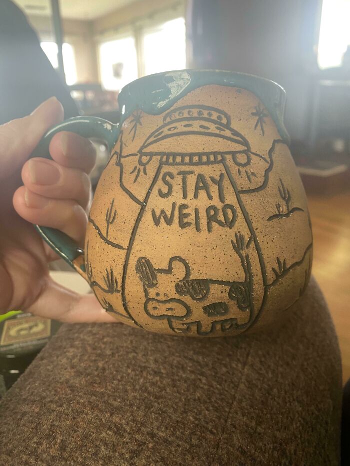 Hand holding a uniquely designed mug with "Stay Weird" text and alien-themed artwork, showcasing creative mug life.