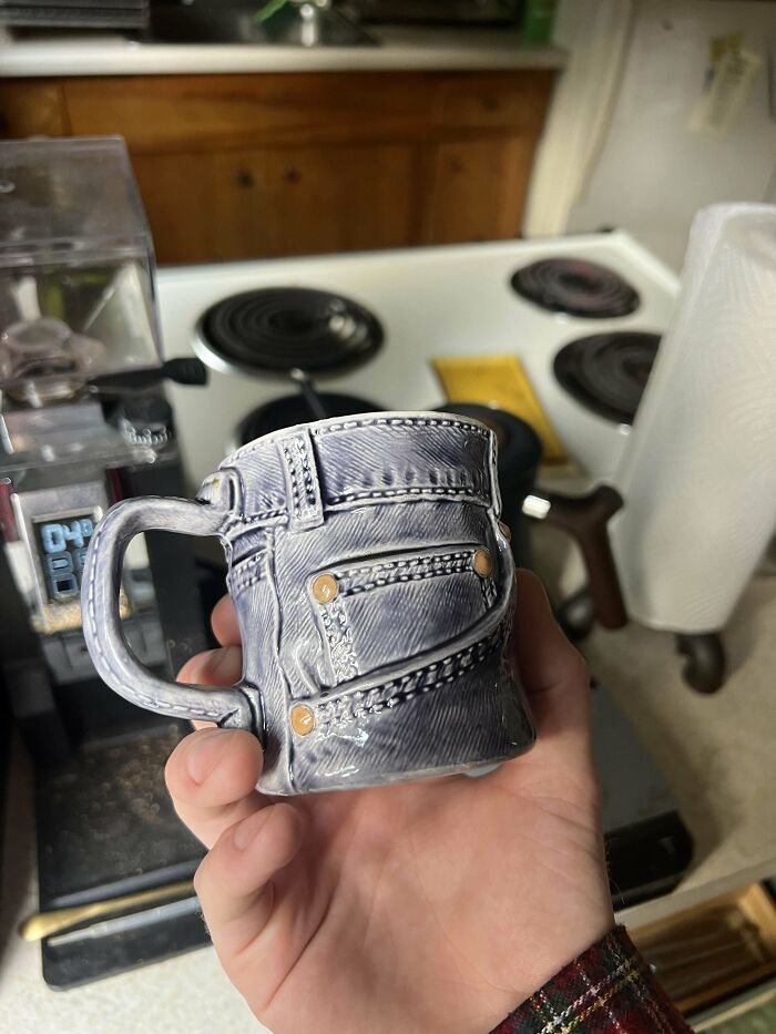 Hand holding a unique denim jeans design mug in a kitchen setting, showcasing creative mug life style.