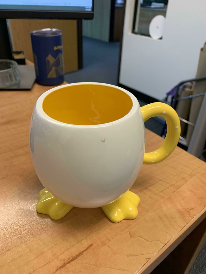 Yellow and white mug with duck feet base and handle on an office desk, showcasing creative mug life design.