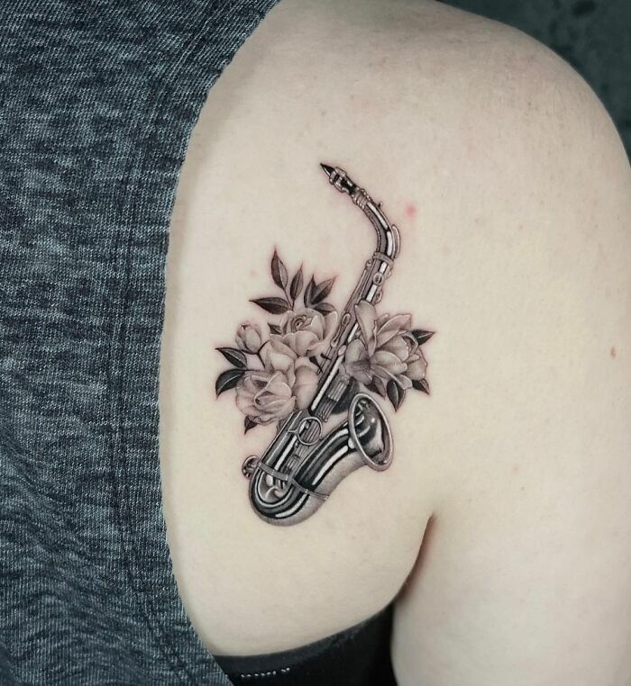 Saxophone tattoo with floral design on upper arm, showcasing a unique music tattoo concept.