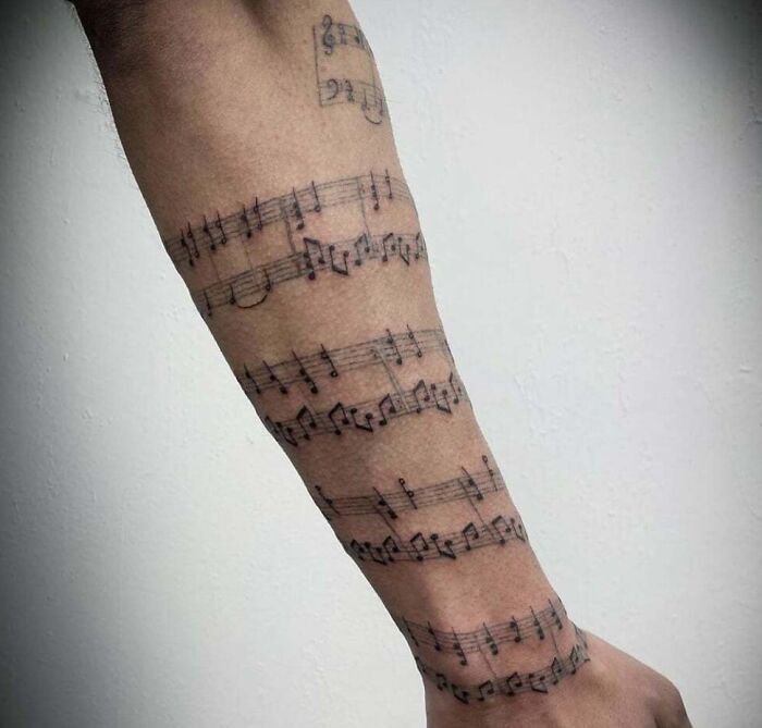 Forearm adorned with intricate music tattoos featuring detailed sheet music notes.