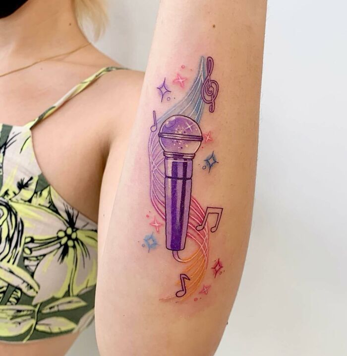 Colorful music tattoo featuring a purple microphone, musical notes, and swirls on a person's arm.