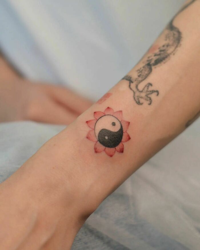 Yin Yang tattoo with a red floral design on forearm, symbolizing duality.