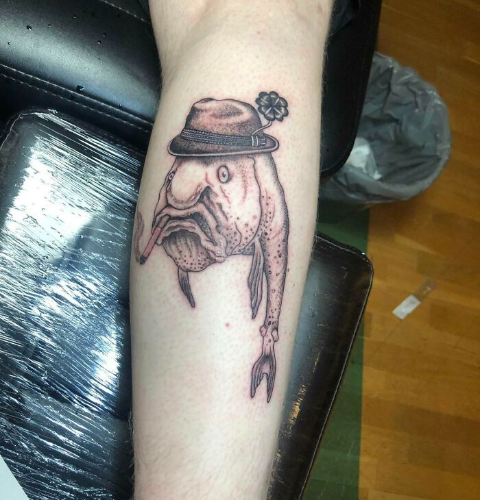 Unusual tattoo of a fish wearing a hat on a person's leg.